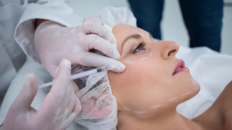 Gloved hands holding a syringe beside the cheek of a woman lying down