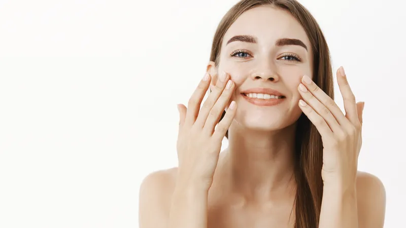 Woman smiling while spreading cream over both cheeks with her fingertips