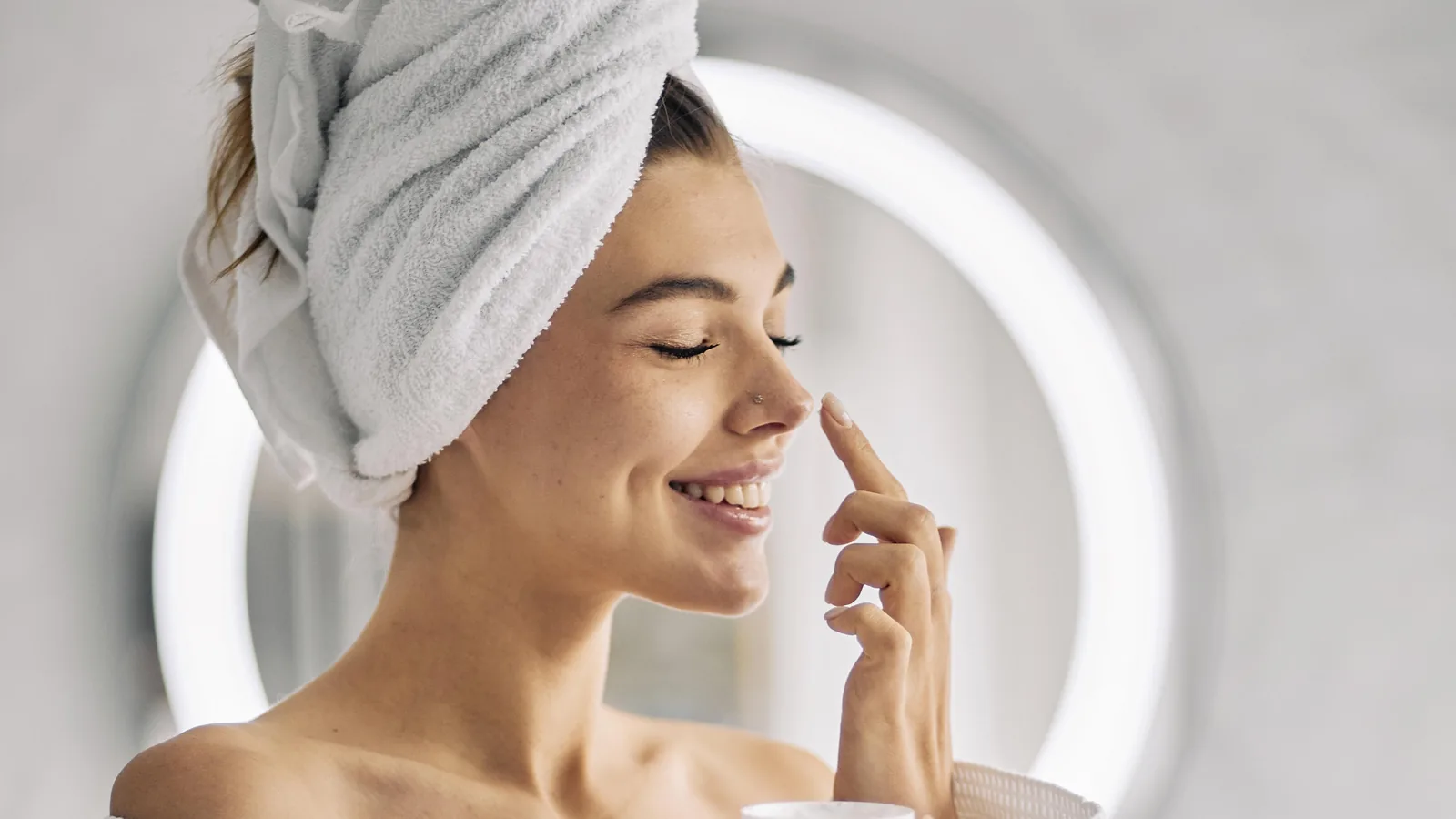 Woman in a bathrobe and towel turban dabbing cream onto her nose