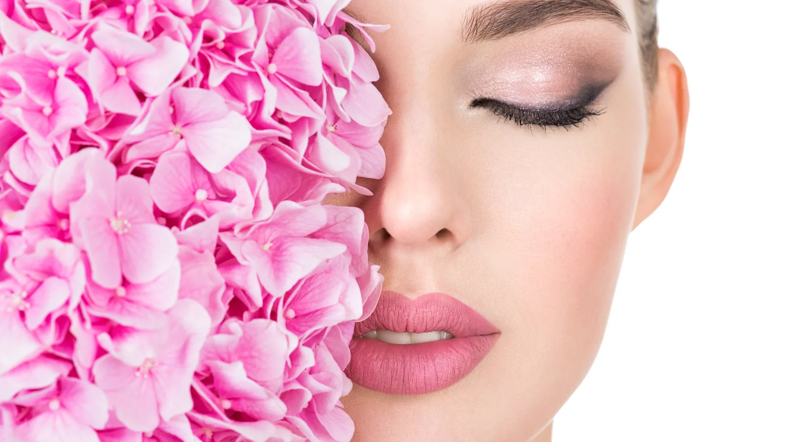 Pink hydrangea blossom covering half of a made-up face